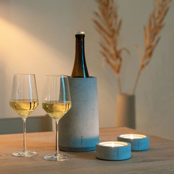 Zwei Gläser Weißwein, eine Weinflasche im Beske Weinkühler „Eiskar“ und zwei brennende Kerzen stehen auf einem Holztisch.