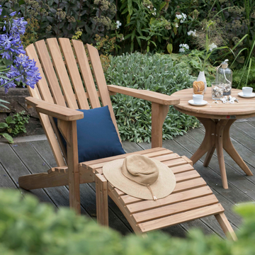 Ein langlebige Gartenlounger Adirondack Montreal und ein runder Tisch stehen im Garten, mit Getränken, Snacks und einer Hütte – stilvoll und wetterfest für entspannte Stunden im Freien.