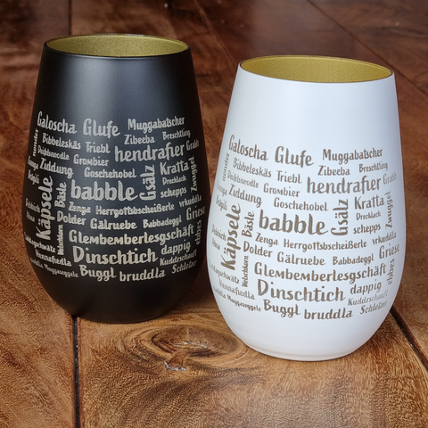 Das Mundart-Windlicht besteht aus zwei Bechern ohne Stiel, einem schwarzen und einem weißen, die jeweils mit deutschen Wörtern in verschiedenen Schriftarten bedruckt sind – ein einzigartiges Glas-Accessoire, gefertigt von einer Manufaktur für Designliebhaber.