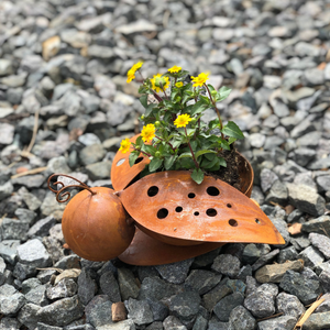 Ein Set aus zwei Edelrost-Marienkäfern mit gelben Blüten steht auf einem Bett aus grauem Kies und ist eine charmante Dekoration für jeden Raum.