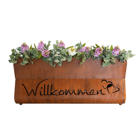 Das Edelrost Pflanzengefäß Bregenz - Willkommen hat einen braunen Rost-Look mit rosa Blumen und „Willkommen“ auf der Vorderseite, perfekt, um Ihrem Raum den Charme des Bayerischen Waldes zu verleihen.