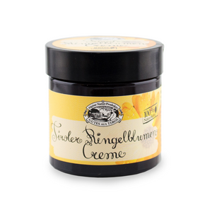 Ein dunkler Tiegel mit der Aufschrift „Ringelblumen Creme“ mit gelbem Etikett und Blumenillustration, ideal für glatte Haut und zur Unterstützung der natürlichen Hautregeneration.