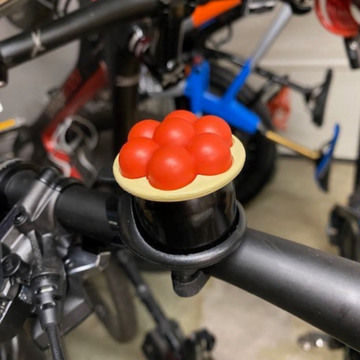 Nahaufnahme eines Fahrradlenkers mit der Schwarzwald Bollenhut Fahrradklingel, einer neuartigen Klingel in Form einer Torte mit roten Beeren, die Ihrer Fahrt authentisches Schwarzwald-Flair verleiht.