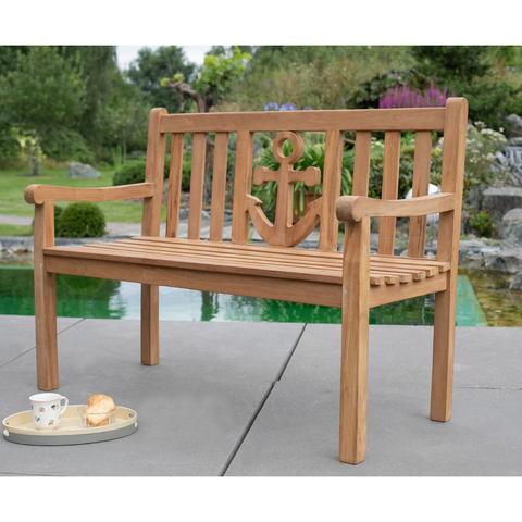 Die Teak-Gartenbank Anker aus massivem Naturholz steht am Pool; daneben ein Tablett mit Tee und Gebäck – stilvolle Outdoor-Möbel für entspannte Stunden im Freien.