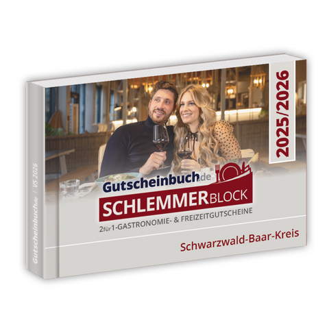 Ein Paar beim Essen und Anstoßen mit dem Gutscheinbuch Kreis Schwarzwald-Baar-Kreis 2026, das attraktive Restaurantangebote und 2-für-1-Gutscheine hervorhebt.