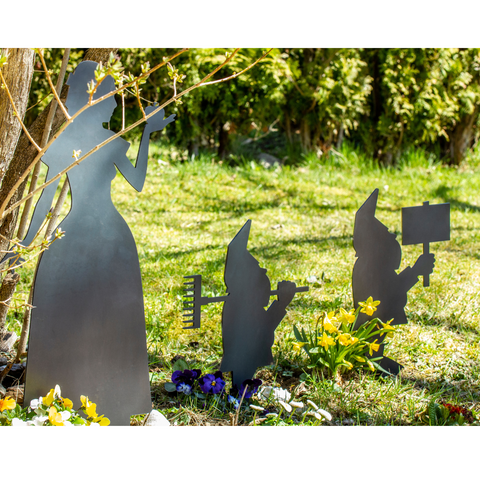 Gartenzwerge aus Stahl stehen zwischen Blumen und Gras im Garten.