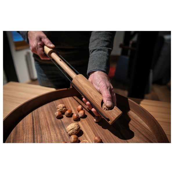 Eine Person knackt mit einem Nussknacker-Nusskracher eine Walnuss über einem Tablett mit verschiedenen Nüssen, inspiriert von den traditionellen Designs von Dietmar Mechsner.