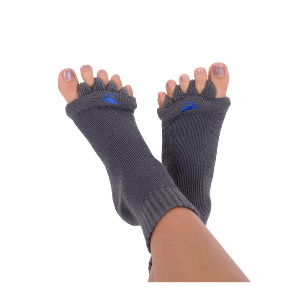 Füße mit grauen Fußausrichtungssocken „Happy Feet“ mit glitzerndem Nagellack vor weißem Hintergrund – ideal als therapeutisches Hilfsmittel zur Linderung von Fußbeschwerden.
