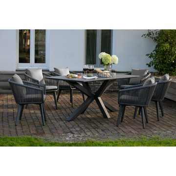 Modernes Gartenmöbelset Rope & Alu mit Tisch und sechs Stühlen, dekorativ mit Blumen, Wein und Speisen auf einer stilvollen Backsteinterrasse arrangiert.