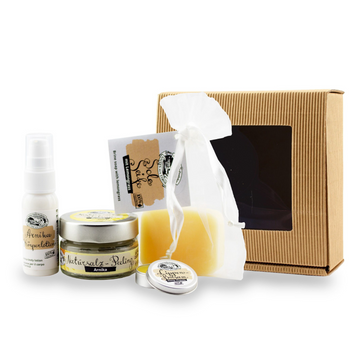 Das Geschenkset „Verwöhn Paket“ beinhaltet eine braune Box, Zitronengras-Pflegespray, Creme, Lippenpflegedose, Natursalz-Peeling-Seife und einen weißen Netzbeutel.
