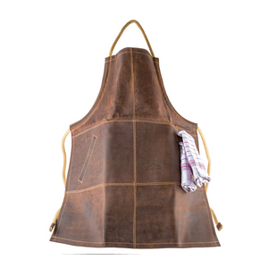 Die Büffelleder-Grillschürze aus braunem Leder verfügt über beige Träger und ein kariertes Handtuch in der Seitentasche, präsentiert auf weißem Hintergrund.