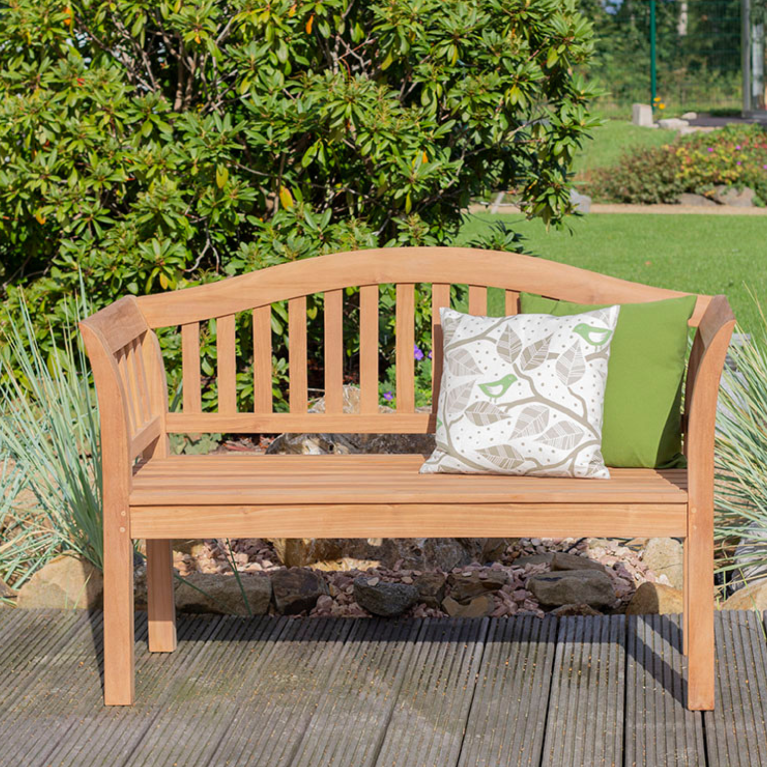 Die Gartenbank Wave aus Massivholz mit zwei gemusterten Kissen bietet stilvolle Sitzgelegenheiten im Grünen – das perfekte Outdoor-Möbel für entspannte Stunden im Garten.