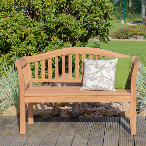 Die Gartenbank Wave aus Massivholz mit zwei gemusterten Kissen bietet stilvolle Sitzgelegenheiten im Grünen – das perfekte Outdoor-Möbel für entspannte Stunden im Garten.
