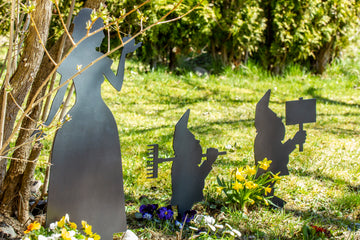 Gartenzwerge aus Stahl stehen zwischen Blumen und Gras im Garten.